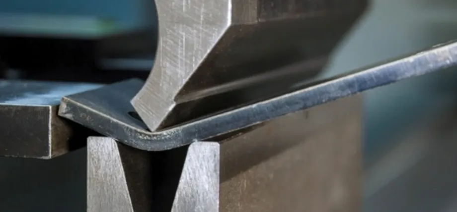 A mechanical press brake bending a thick metal strip into a V-shape, capturing the precise moment of deformation between the die and punch.