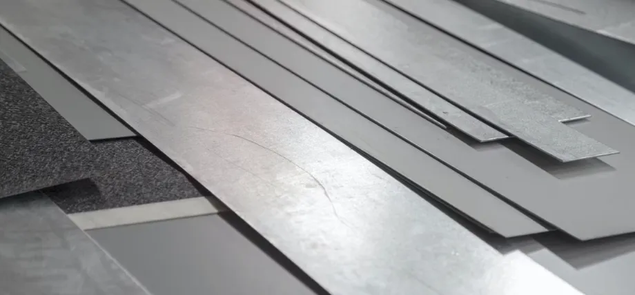 A collection of various raw sheet metal strips and industrial metal materials stacked together for production