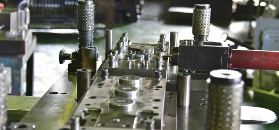 A metal strip showcasing successive stages of a progressive stamping sequence alongside the finalized D-shaped components.