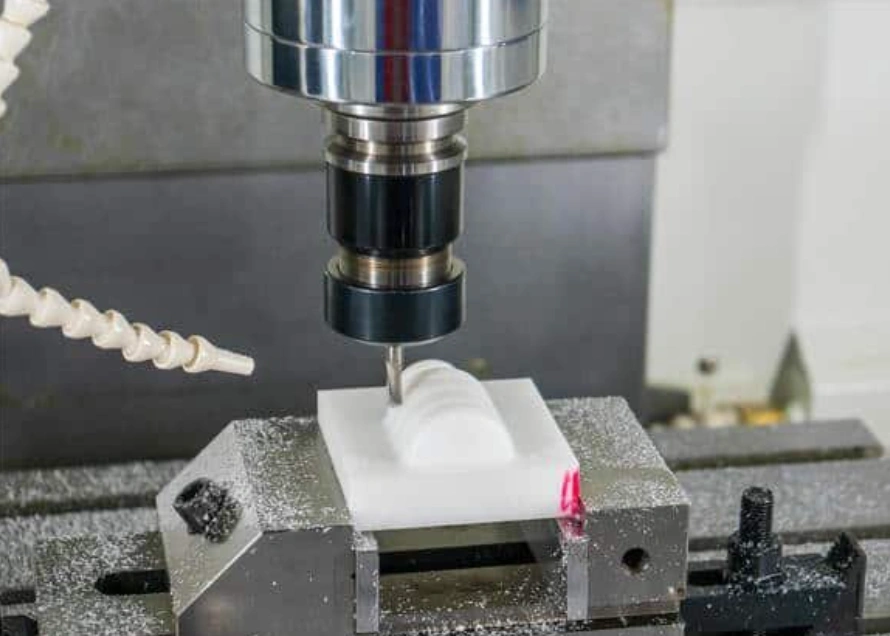 CNC milling machine cutting a white plastic block prototype on a metal workholding fixture.