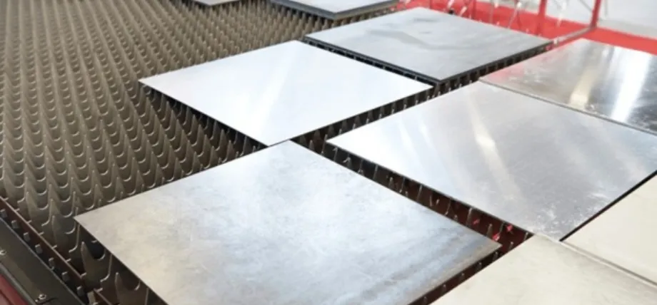 Several square metal plates resting on a spiked laser cutting bed, ready for high-precision industrial processing