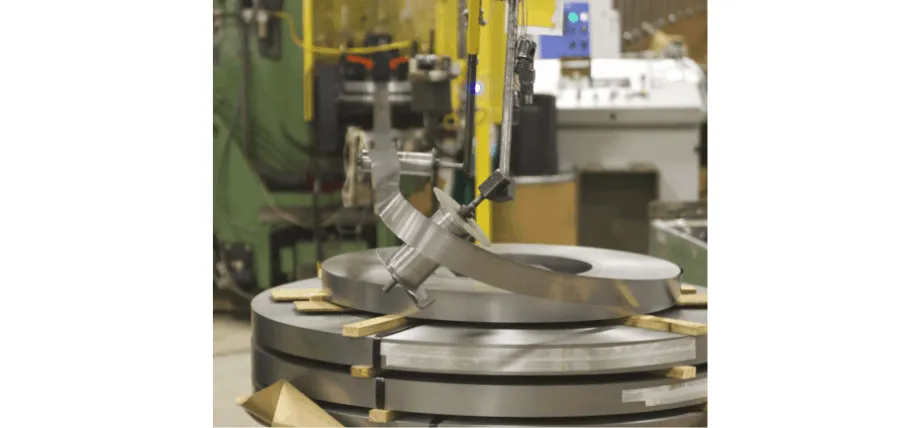 Large rolls of raw sheet metal coil fed systematically into automated manufacturing machinery via an overhead mechanical arm