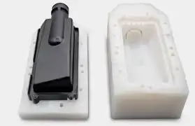 Black plastic housing placed beside a white mold cavity used for injection molding.