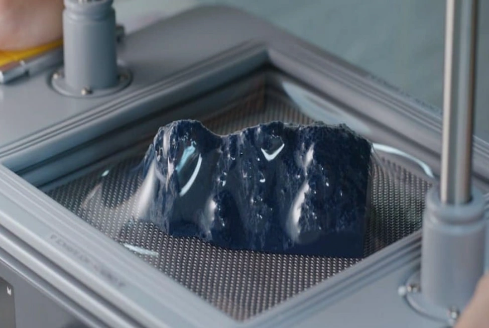 Dark thermoplastic sheet vacuum-formed over a mold on a perforated forming table, showing draped material conforming to the mold shape
