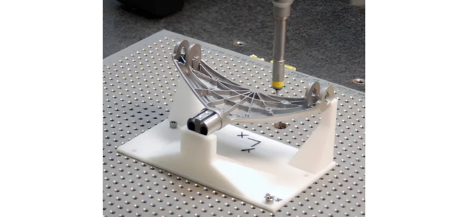 A CMM probe inspects a complex, curved aerospace or automotive aluminum component held on a white 3D-printed custom fixture.