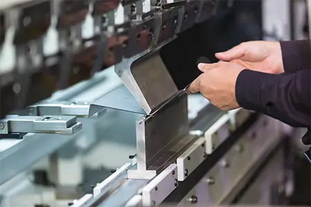 Technician shaping a metal sheet on a press brake machine.