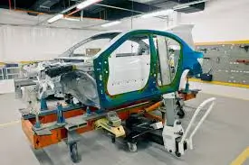 Car body frame mounted on supports inside an automotive production facility.
