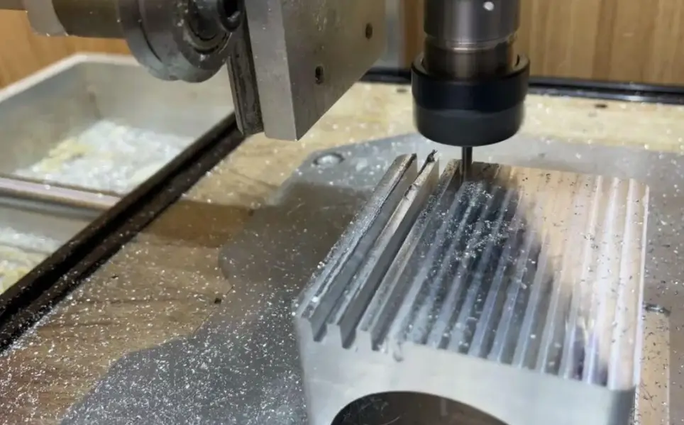 CNC end mill cutting parallel fins into an aluminum heat sink with chips scattered across the machine bed. 