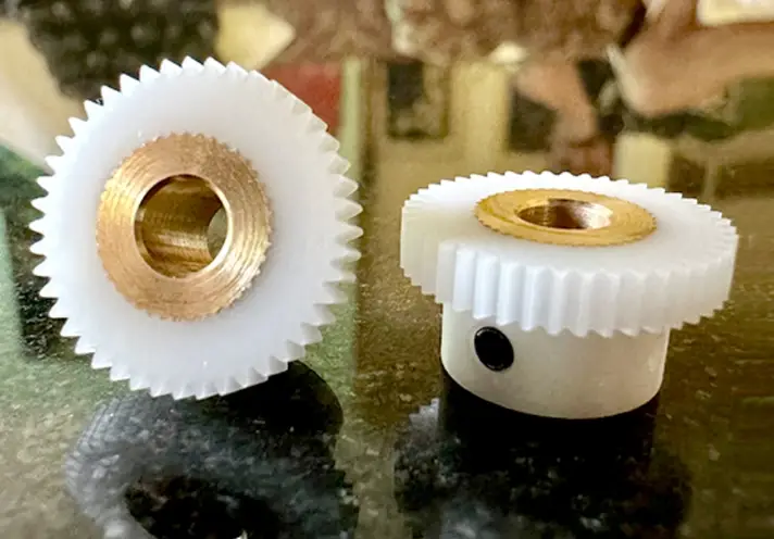 Two white Delrin spur gears with brass center bushings on a reflective glass surface.  