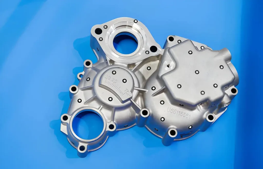 The image shows a magnesium automotive engine cover displayed against a blue background. 
