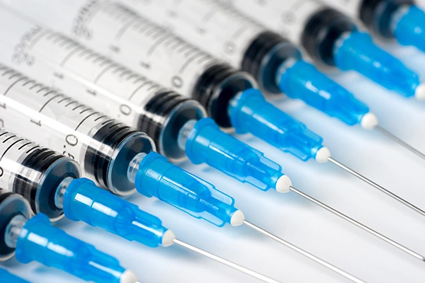Row of medical syringes with blue needle caps lined up closely