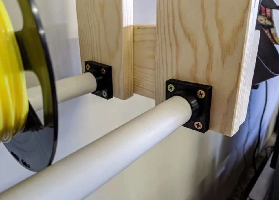 White pipes secured through black drilled PVC bracket fittings screwed into a wooden frame.