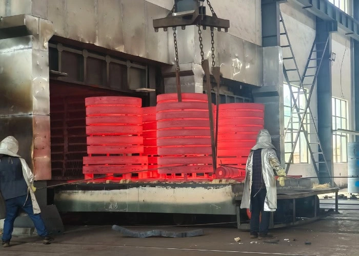 Workers removing red-hot metal rings from a large heat treatment furnace