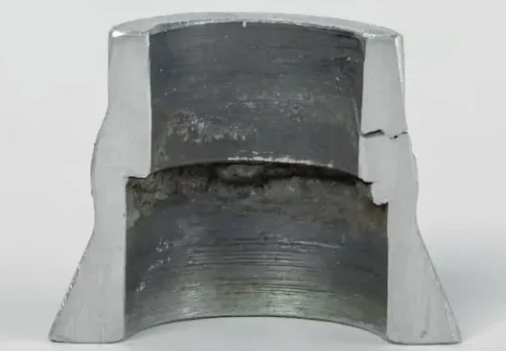 Cross-sectioned aluminum part showing severe internal corrosion and delamination along a horizontal fracture plane 