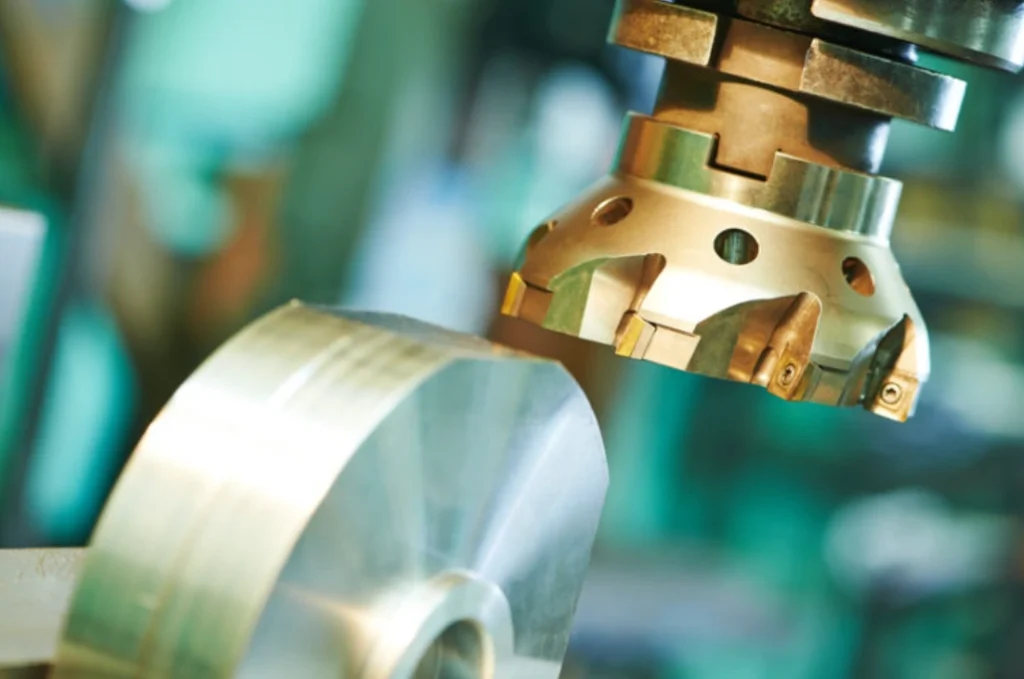 Close-up of a carbide indexable face mill with inserted cutting tips engaging a metal workpiece on a CNC milling machine
