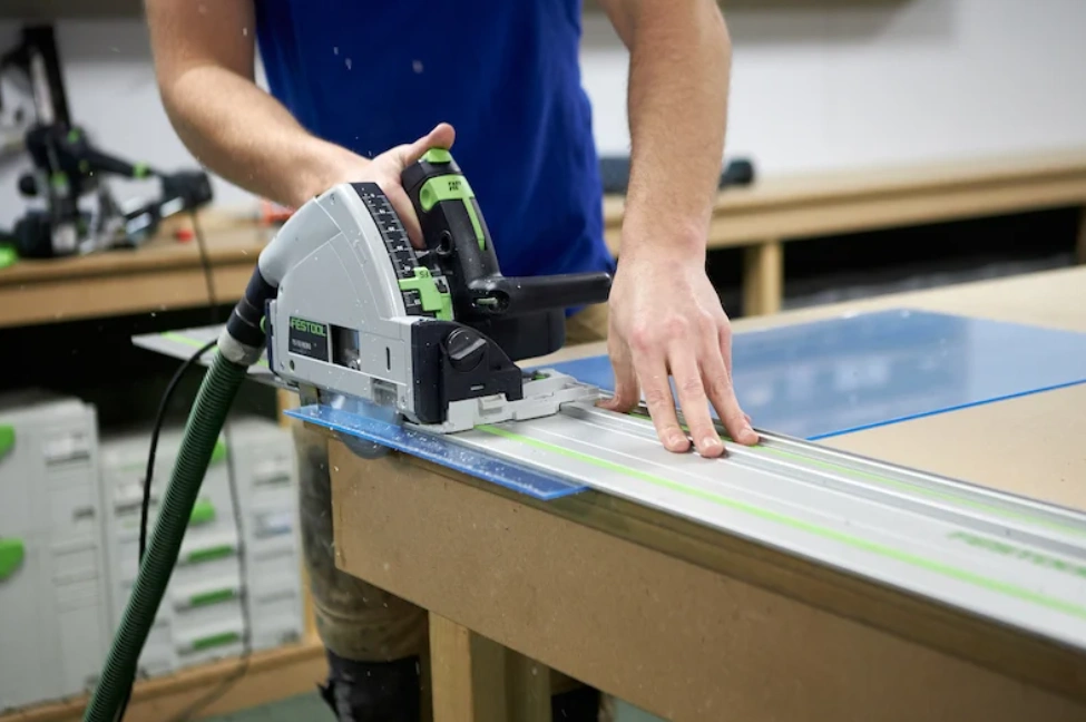 Person using a track saw to cut a blue-masked polycarbonate sheet on a workbench.