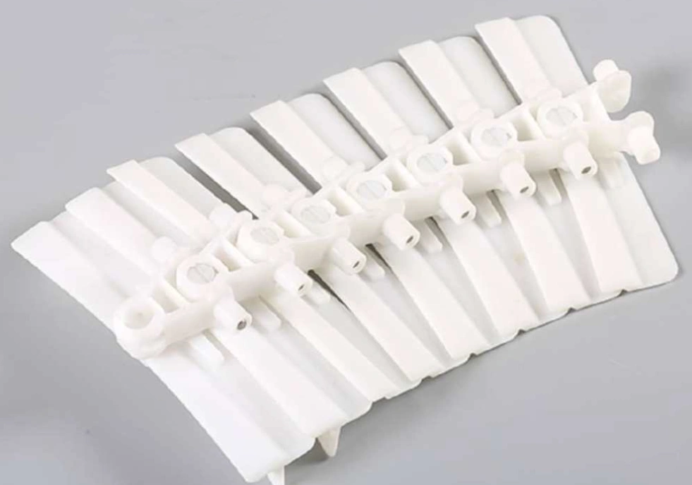 White Delrin modular conveyor chain links arranged on a gray surface.