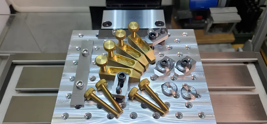An assortment of brass toe clamps, steel bolts, and positioning blocks arranged on a silver grid fixture plate.