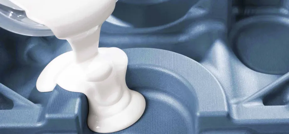 Close-up of white liquid polyurethane resin being poured into a blue textured mold cavity.