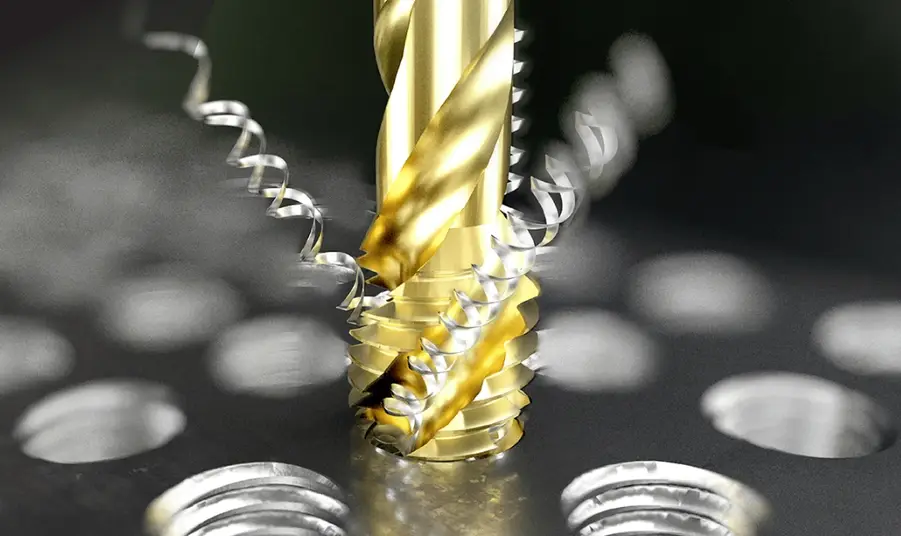 Gold-colored tap cutting threads into a metal workpiece with swarf chips visible