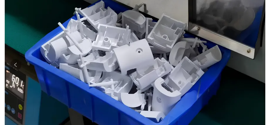 A blue plastic storage bin filled with white, custom-molded plastic prototype components freshly produced in a manufacturing facility.