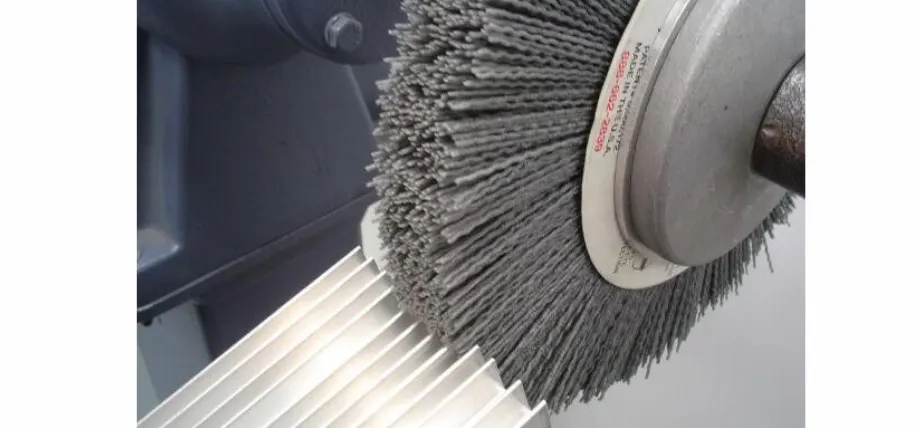 A gray abrasive wire wheel brush finishing the surface of a multi-finned aluminum heat sink.