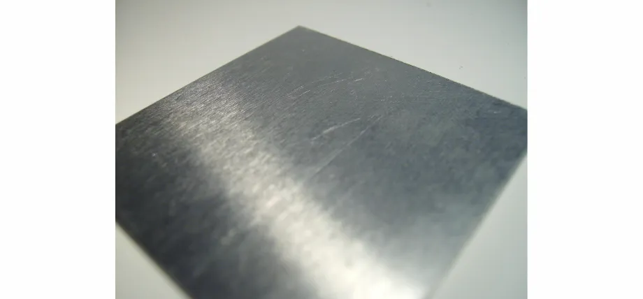 Close-up of a square metal plate with a consistent linear brushed texture reflecting light.