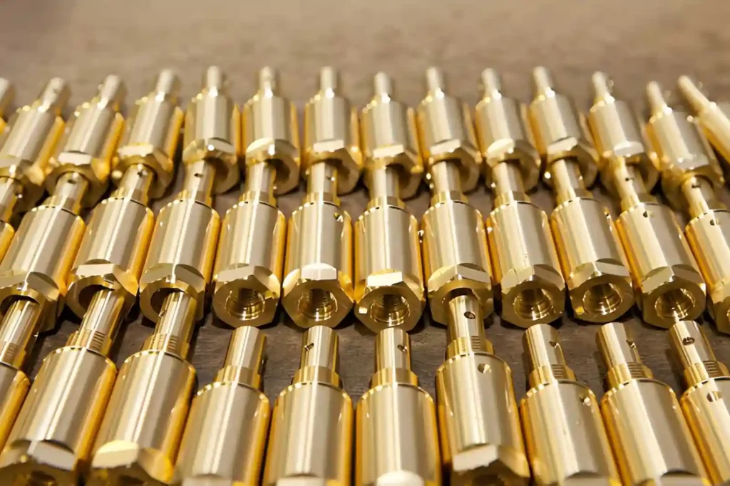The image shows custom brass parts with machined surfaces arranged on a factory floor. Brass can handle moderate loads, but it is less suitable for applications involving high stress or heavy mechanical forces.