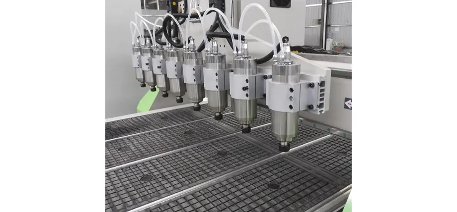 An industrial multi-spindle machine setup featuring a row of eight vertical machining heads positioned above a gridded vacuum bed.