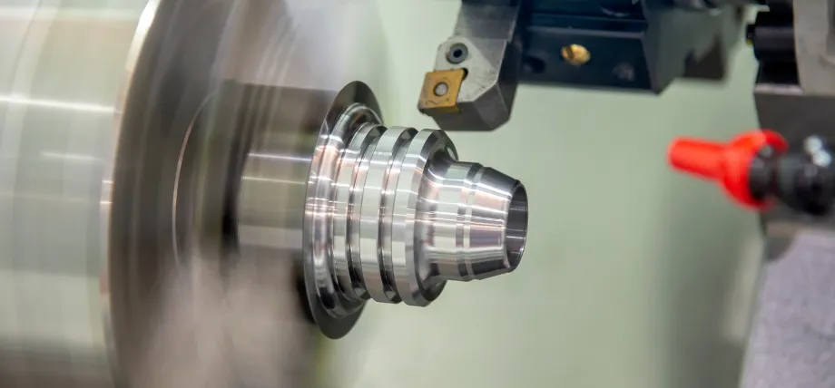 A close-up of a CNC lathe machine cutting precise external grooves into a rapidly spinning cylindrical metal workpiece.