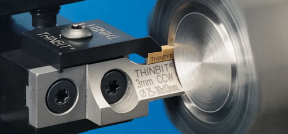 A Thinbit face grooving tool with a carbide insert engaged in precision machining on a rotating metal piece against a blue background.