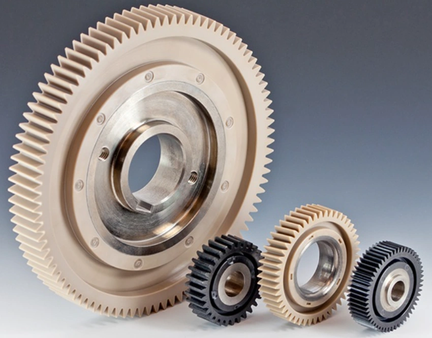 Large machined PEEK spur gear with metal hub alongside smaller carbon-filled PEEK automotive gears