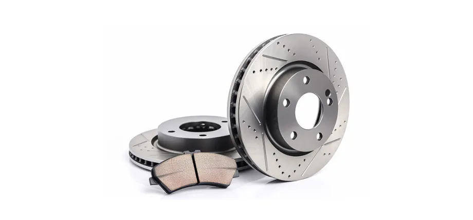 Two slotted and drilled silver steel automotive brake rotors paired with a high-performance brake pad on a white background.