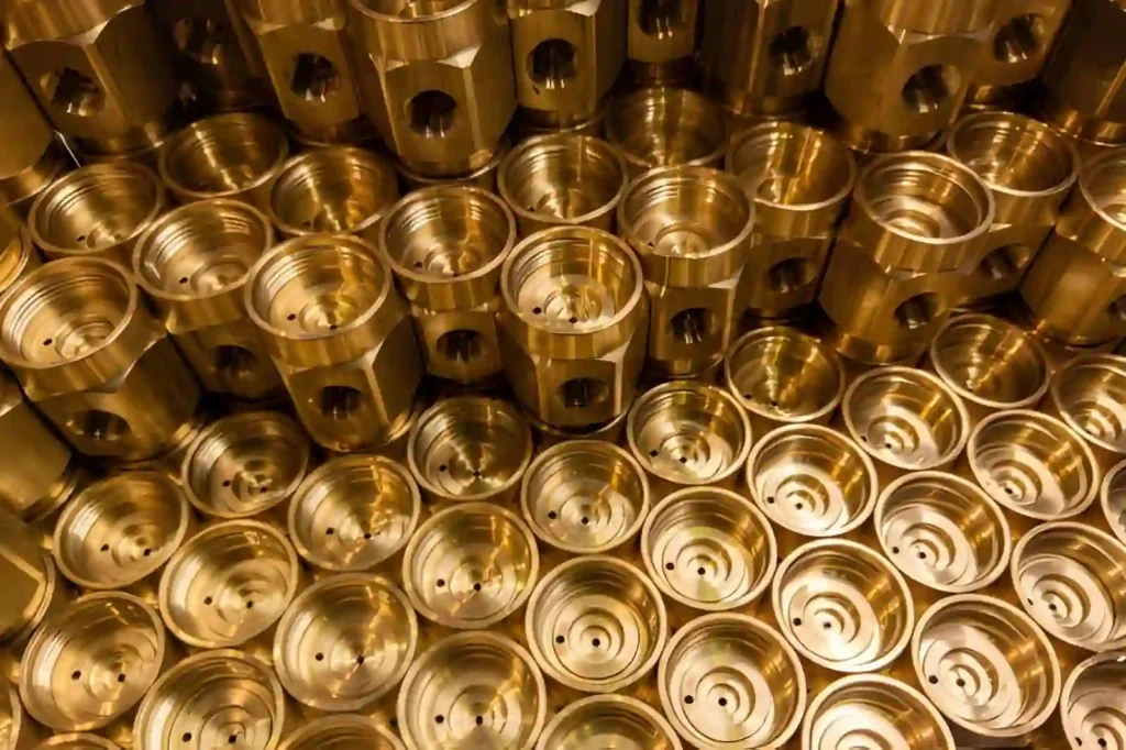 The image shows a collection of shiny, brass-machined parts arranged in bulk.