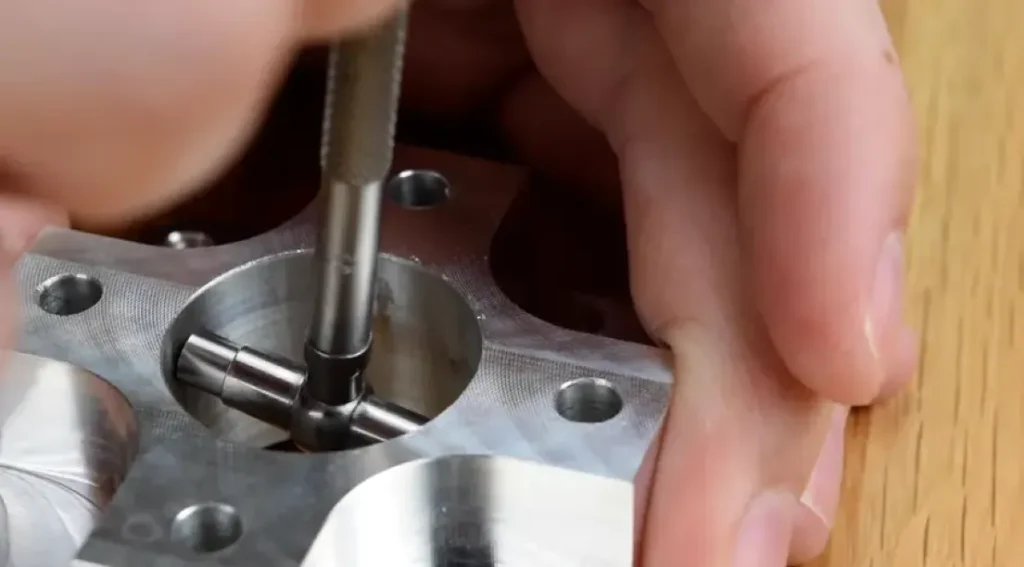 A person’s hand holding/measuring a bored hole in a machined aluminum part using a bore gauge.