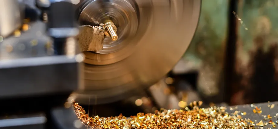 A high-speed lathe machining a brass component, producing a large volume of small, golden-colored metal chips.