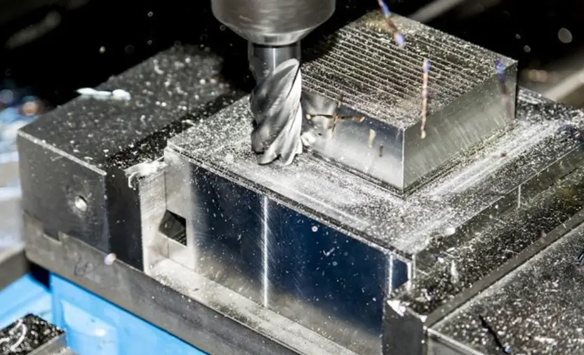  End mill roughing a metal block securely clamped in a machine vise, with chips scattered across the fixture. 
