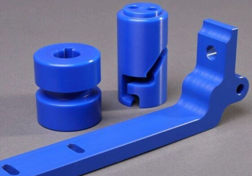 Three blue Delrin (acetal) CNC-machined parts — coupling, cylindrical clamp, and mounting bracket