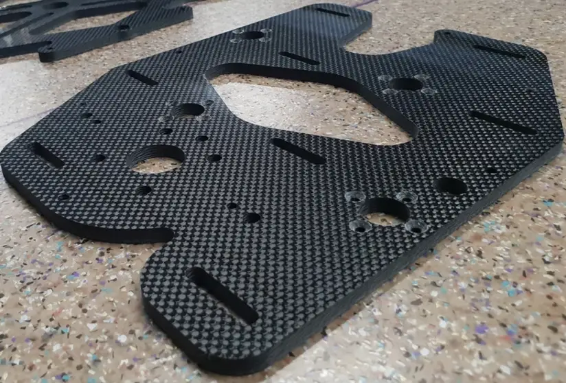 CNC-machined carbon fiber plate with routed slots, drilled holes, and contoured cutouts