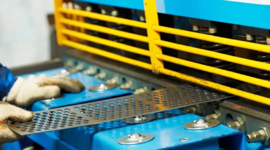 Gloved worker feeding a perforated metal sheet through an industrial deburring machine to smooth laser-cut edges. 