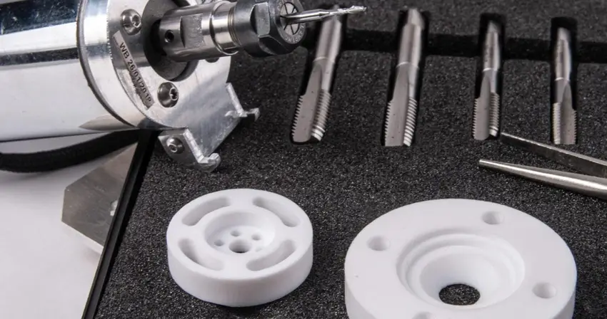 Sharp cutting tools and tap set beside two precision-machined white PTFE disc components.