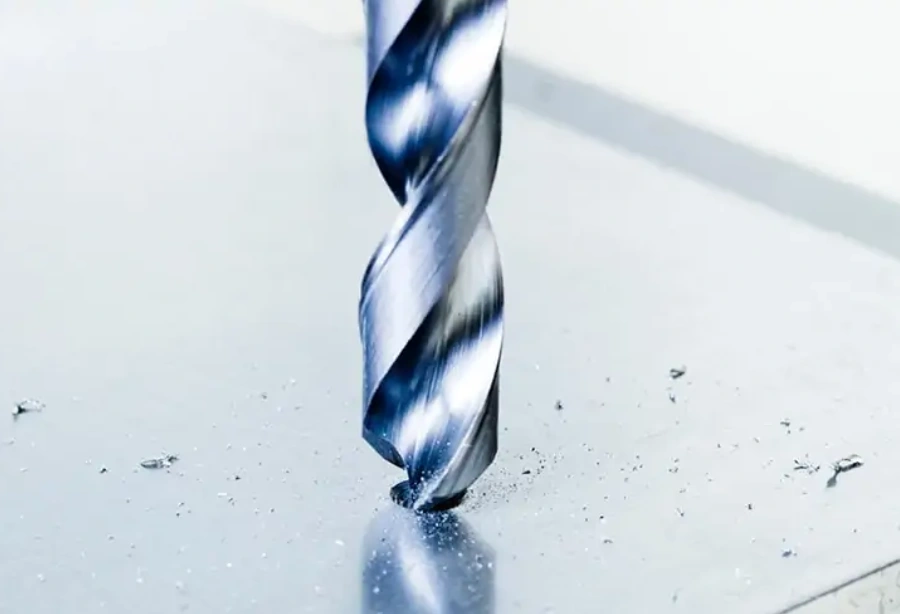 Close-up of a coated twist drill bit spot drilling into a metal surface with chips scattered around the entry point