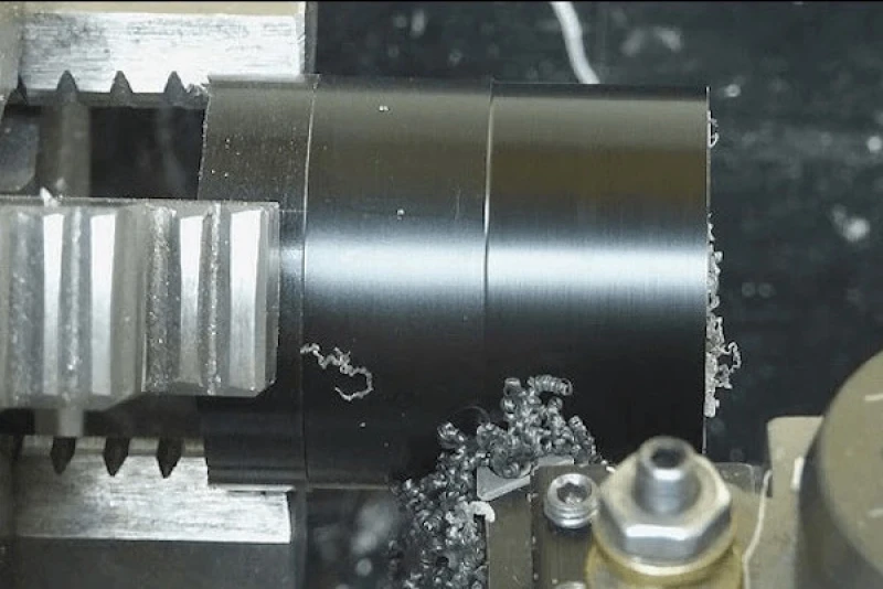 CNC lathe turning black acetal cylinder, producing curled machining chips
