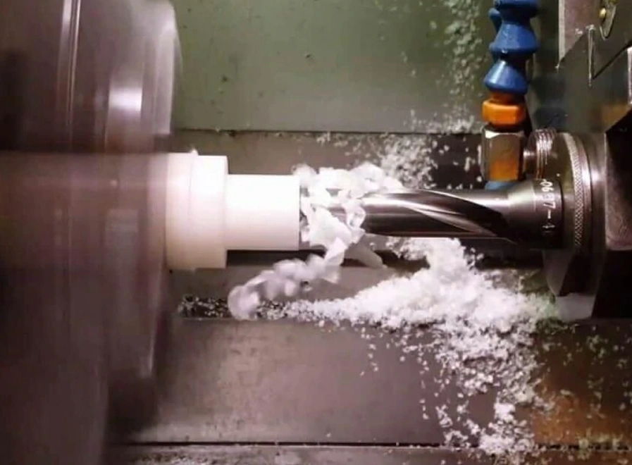 Drill bit boring into white ABS rod, curling ribbon-like chips forming