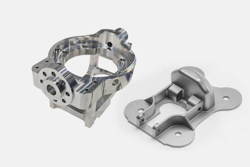 Two precision-milled aerospace aluminum components with intricate bracket and housing geometry