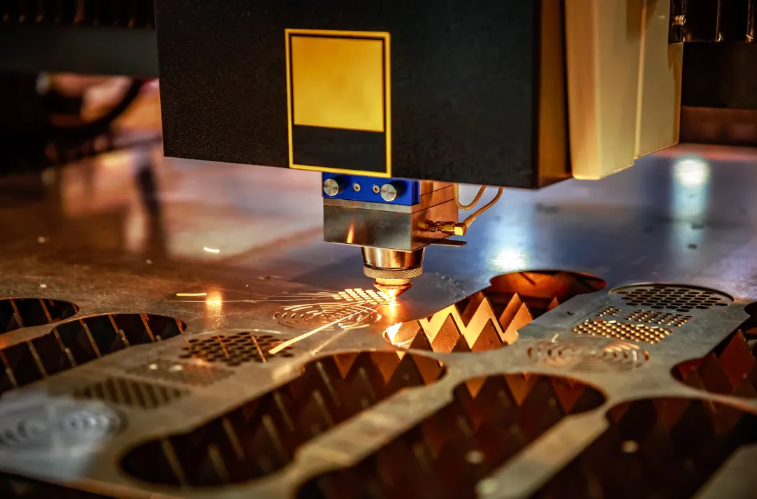 Fiber laser cutting head cutting zigzag pattern into perforated copper sheet metal, close-up with sparks