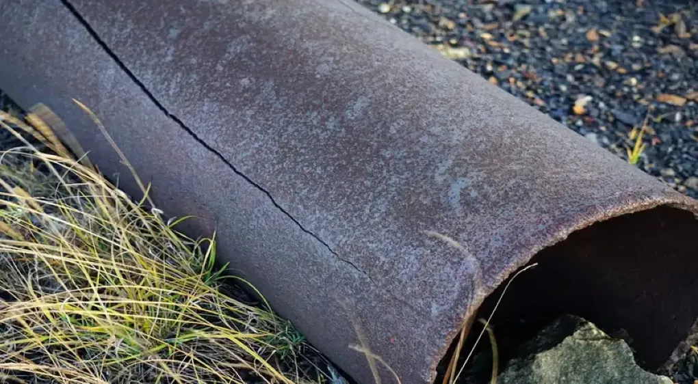 Rusted metal pipe with a longitudinal stress corrosion crack, lying in grass  