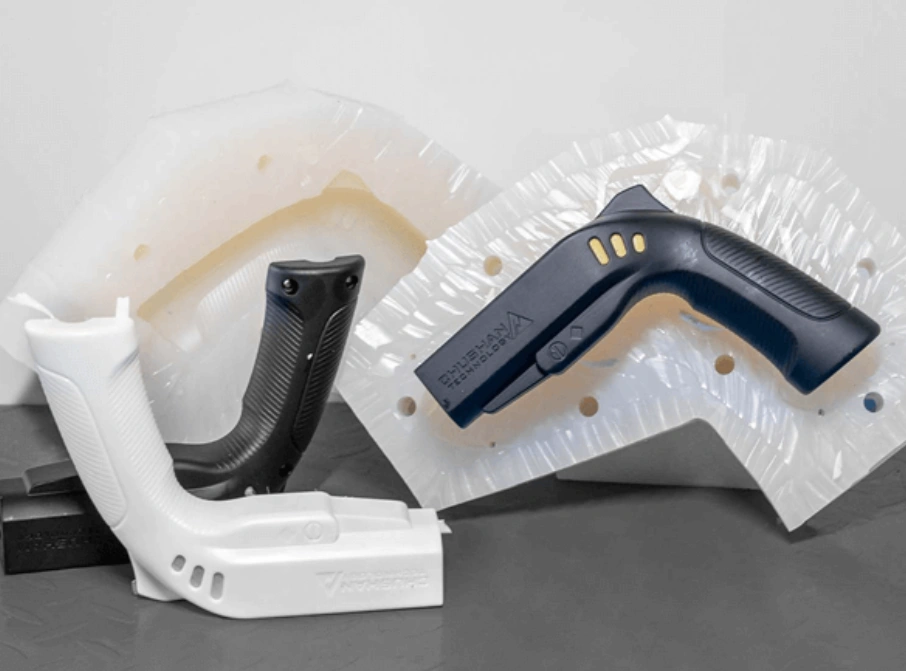 Injection-molded pistol-grip housings in white and black plastic, wrapped and unwrapped, on a table.