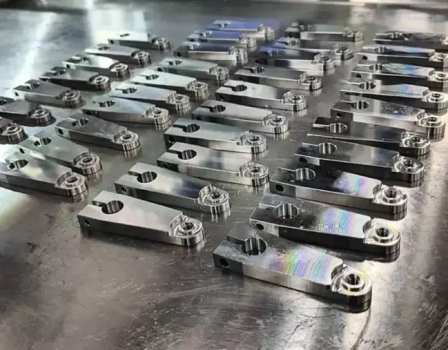 Batch of low-volume CNC-machined metal brackets with threaded holes laid on a work table.