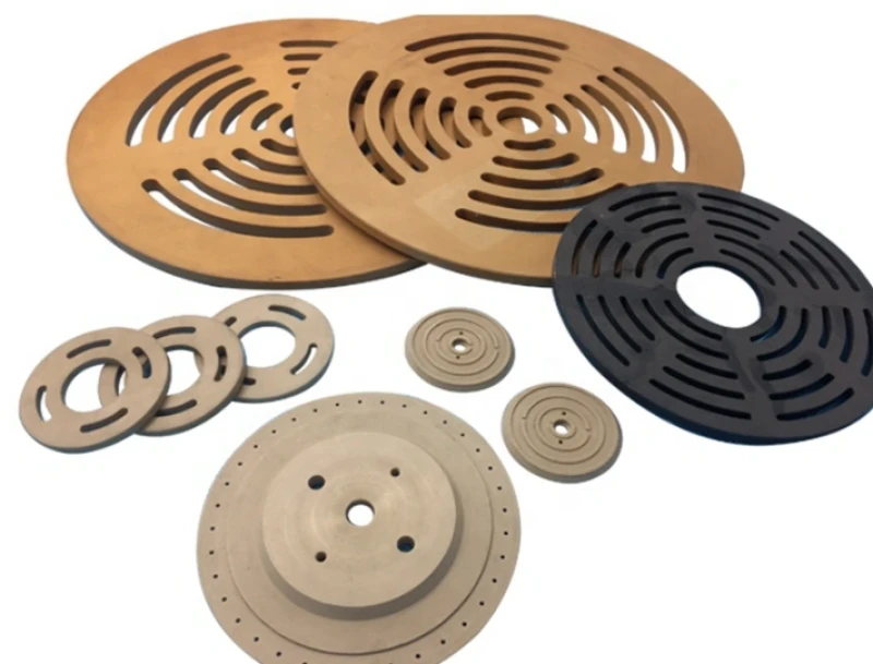 Machined PEEK discs and rotors in tan and black, showing slotted and drilled patterns
